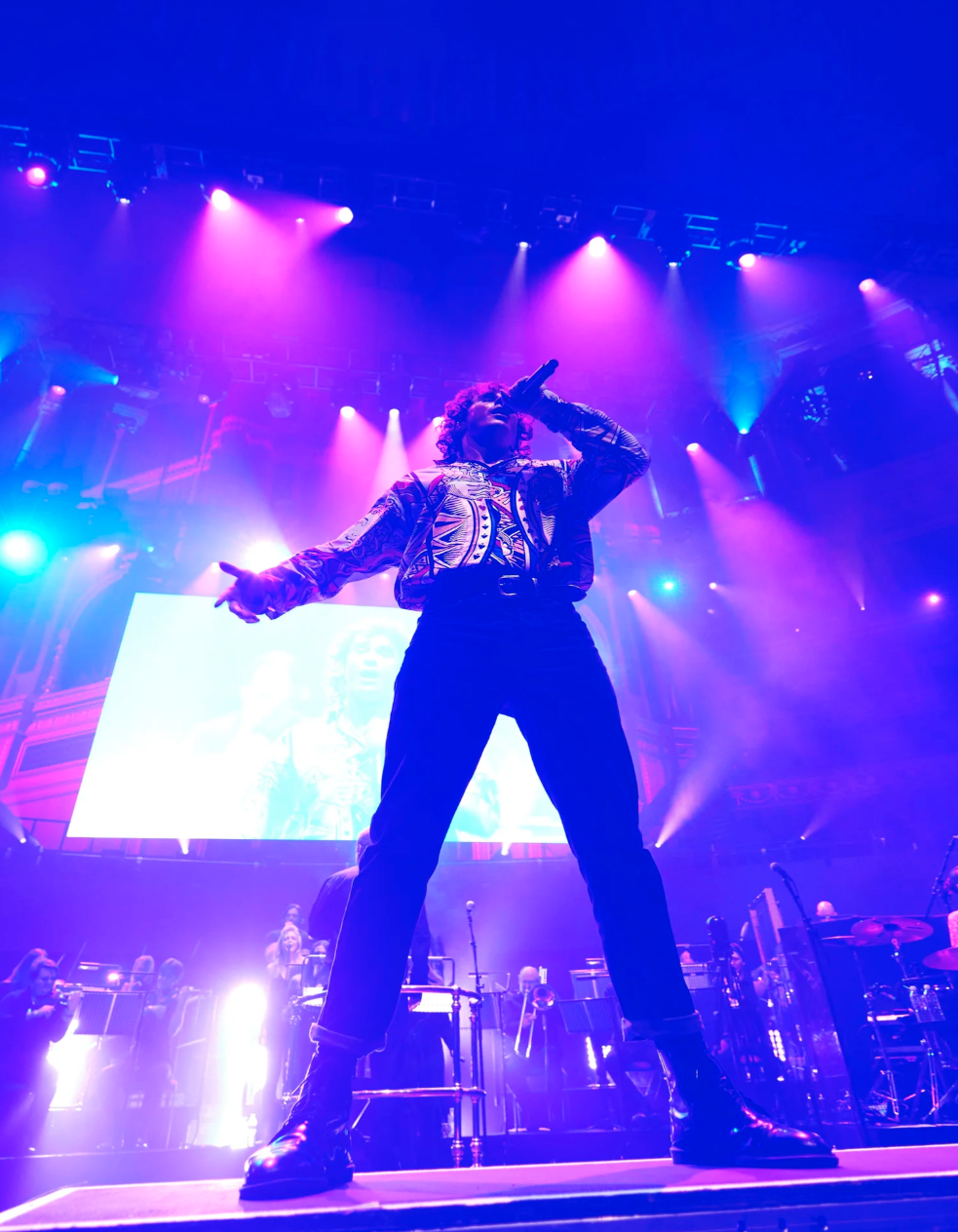 A performer on stage bends backwards during an energetic concert performance with dramatic blue and pink lighting.