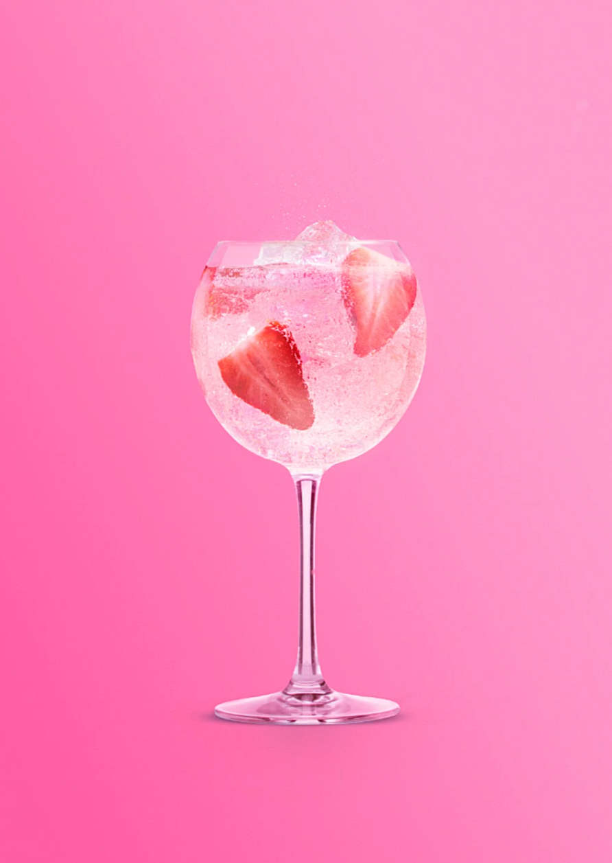 Pink cocktail with strawberry garnish in a coupe glass against vibrant pink background.