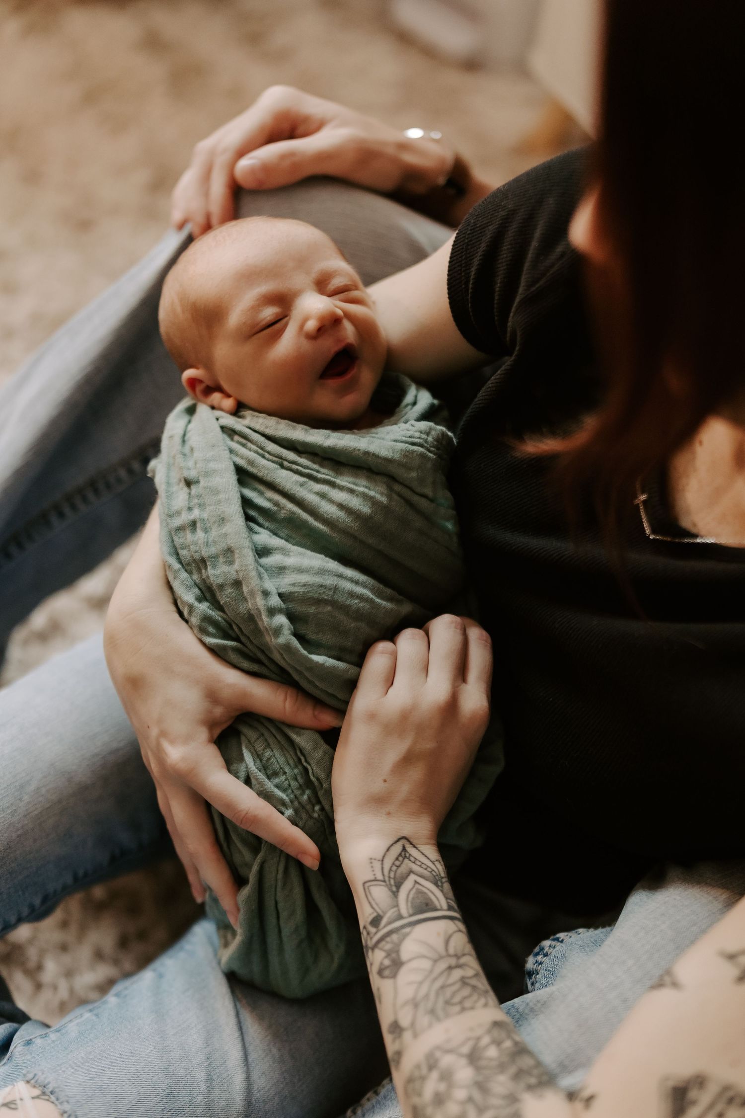 Intimate portrait of newborn baby being held in sage green swaddle wrap.