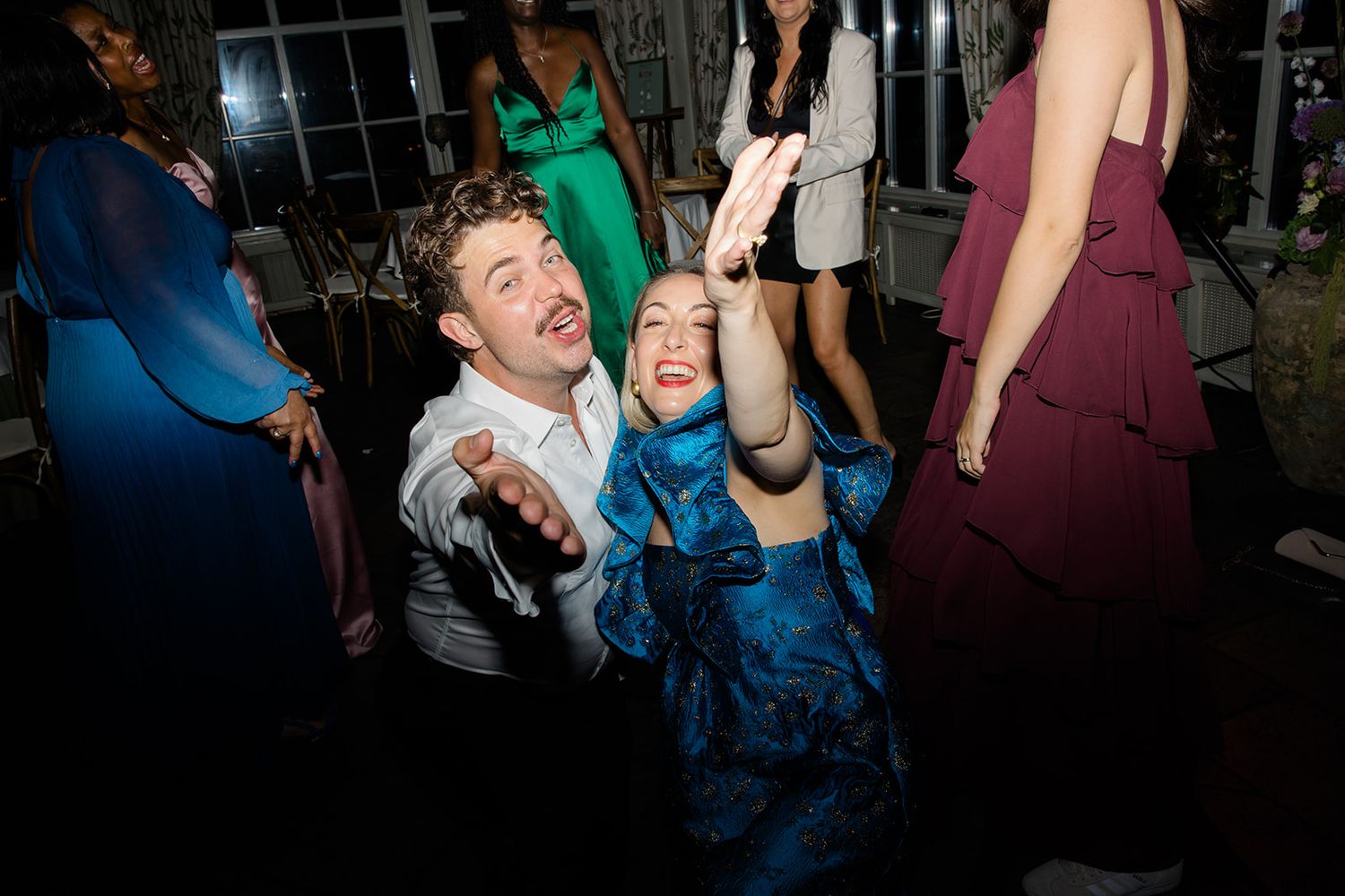 Two people dance enthusiastically together on a dark dance floor at what appears to be a party or celebration.