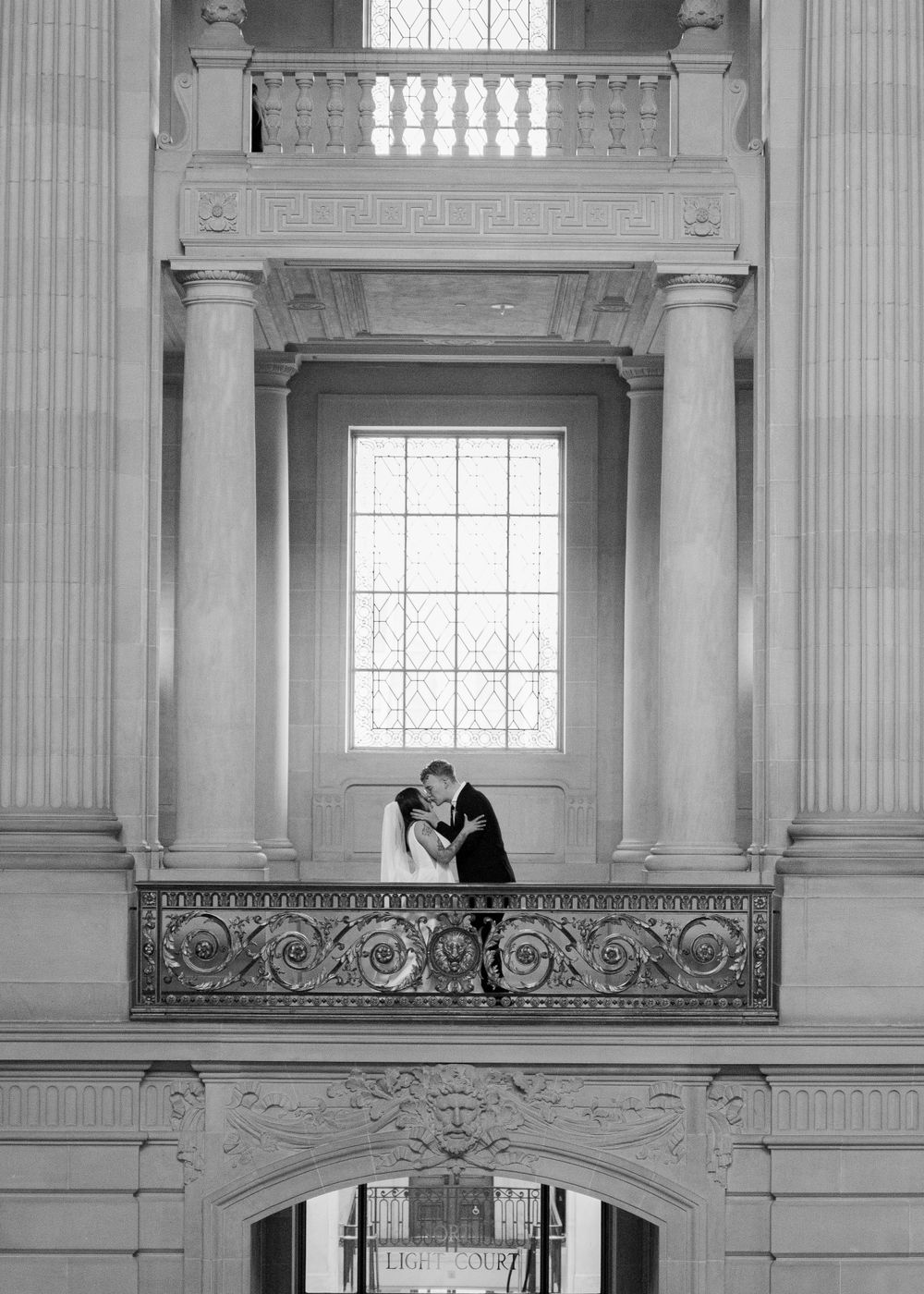 A black and white wedding photo captured through an ornate architectural frame at City Hall.