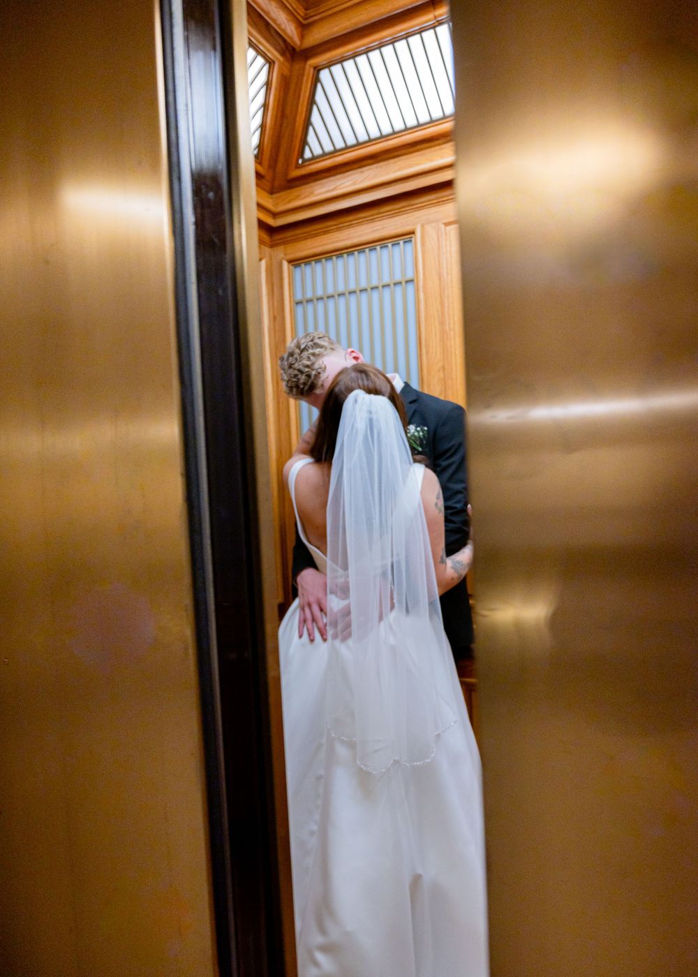 A wedding kiss captured through an elevator doorway.
