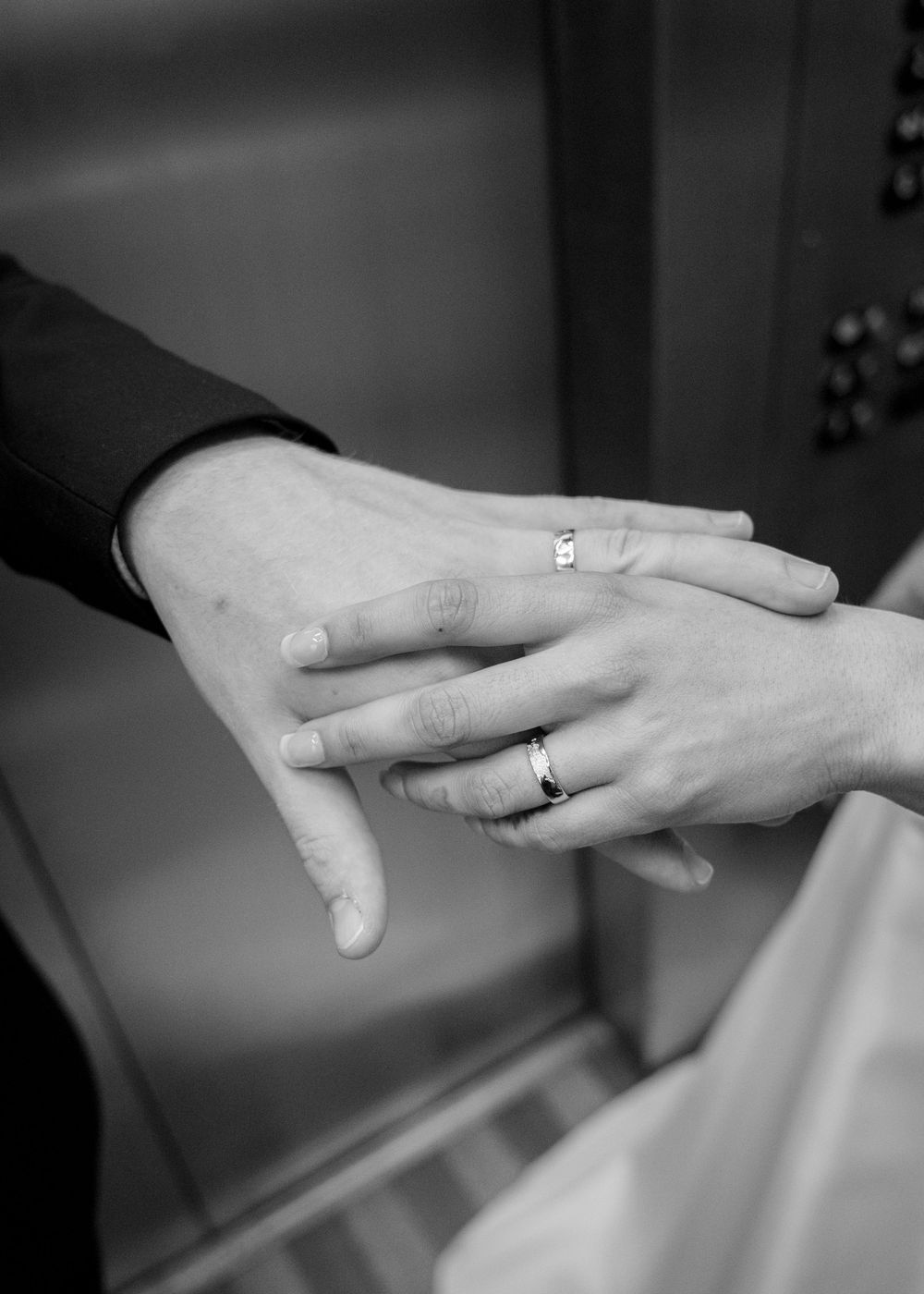 Black and white photograph of hands displaying engagement and wedding rings on fingers.