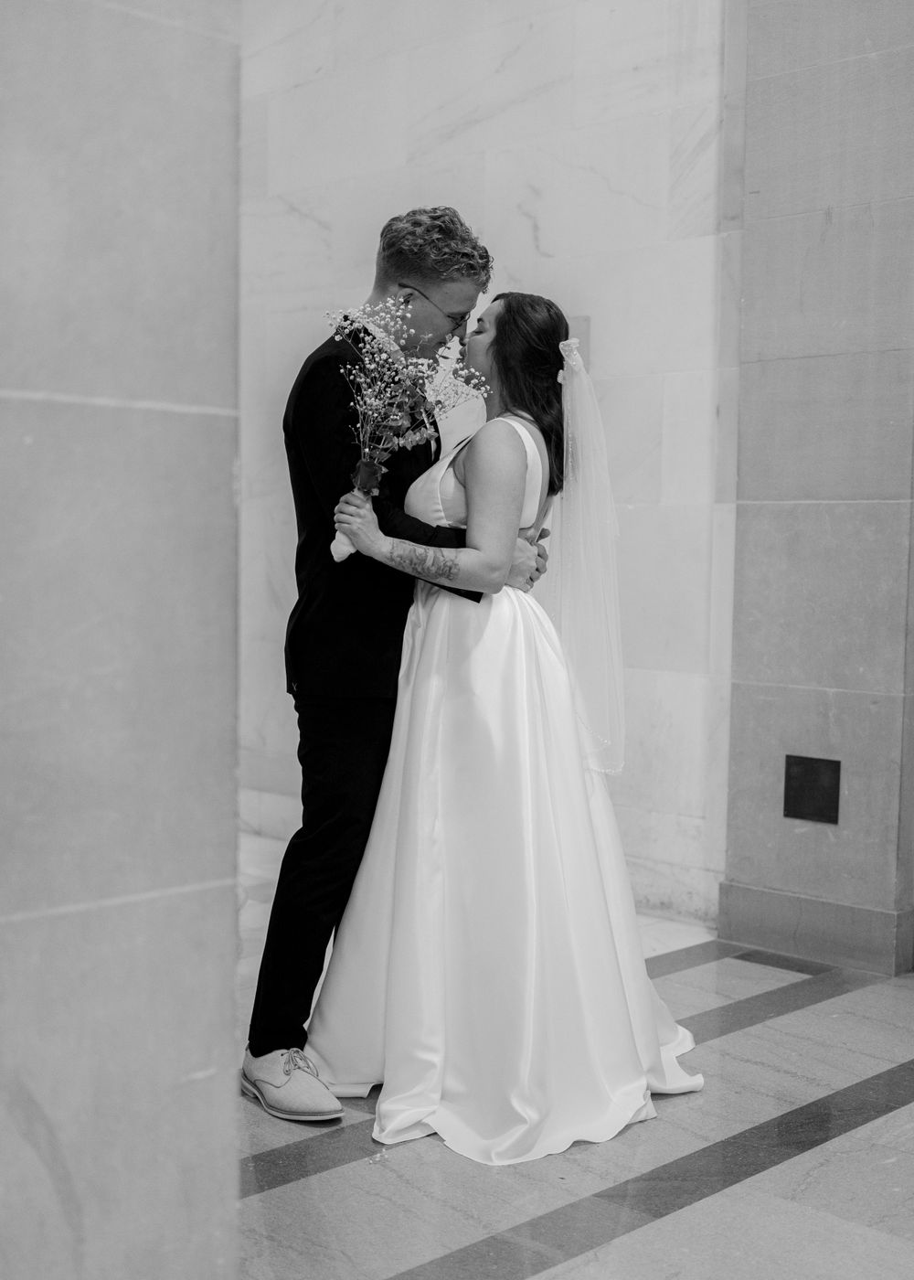 A romantic black and white wedding portrait of a couple embracing in front of a white wall.