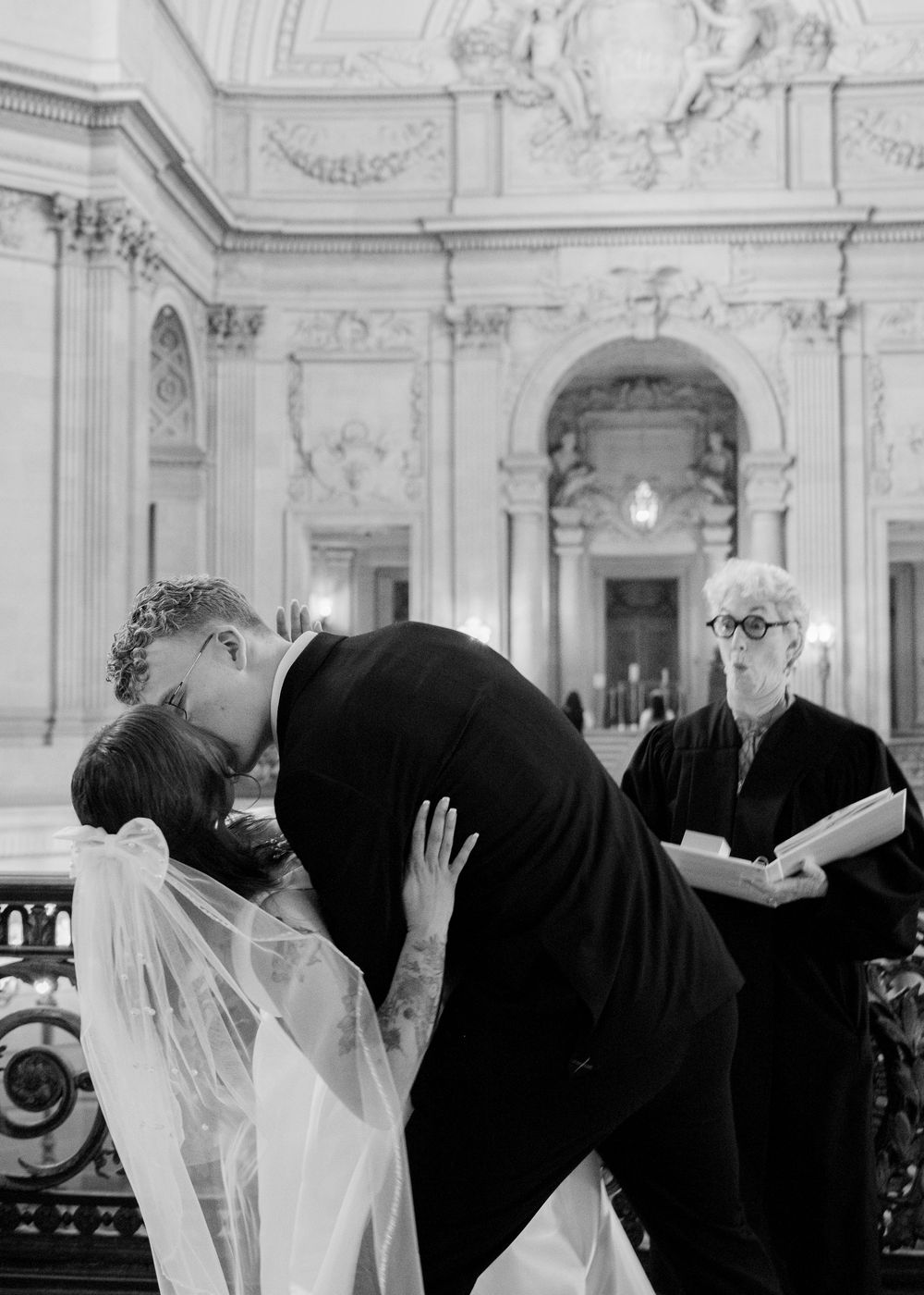A black and white wedding ceremony moment captured in a grand historic venue with classical architectural features.