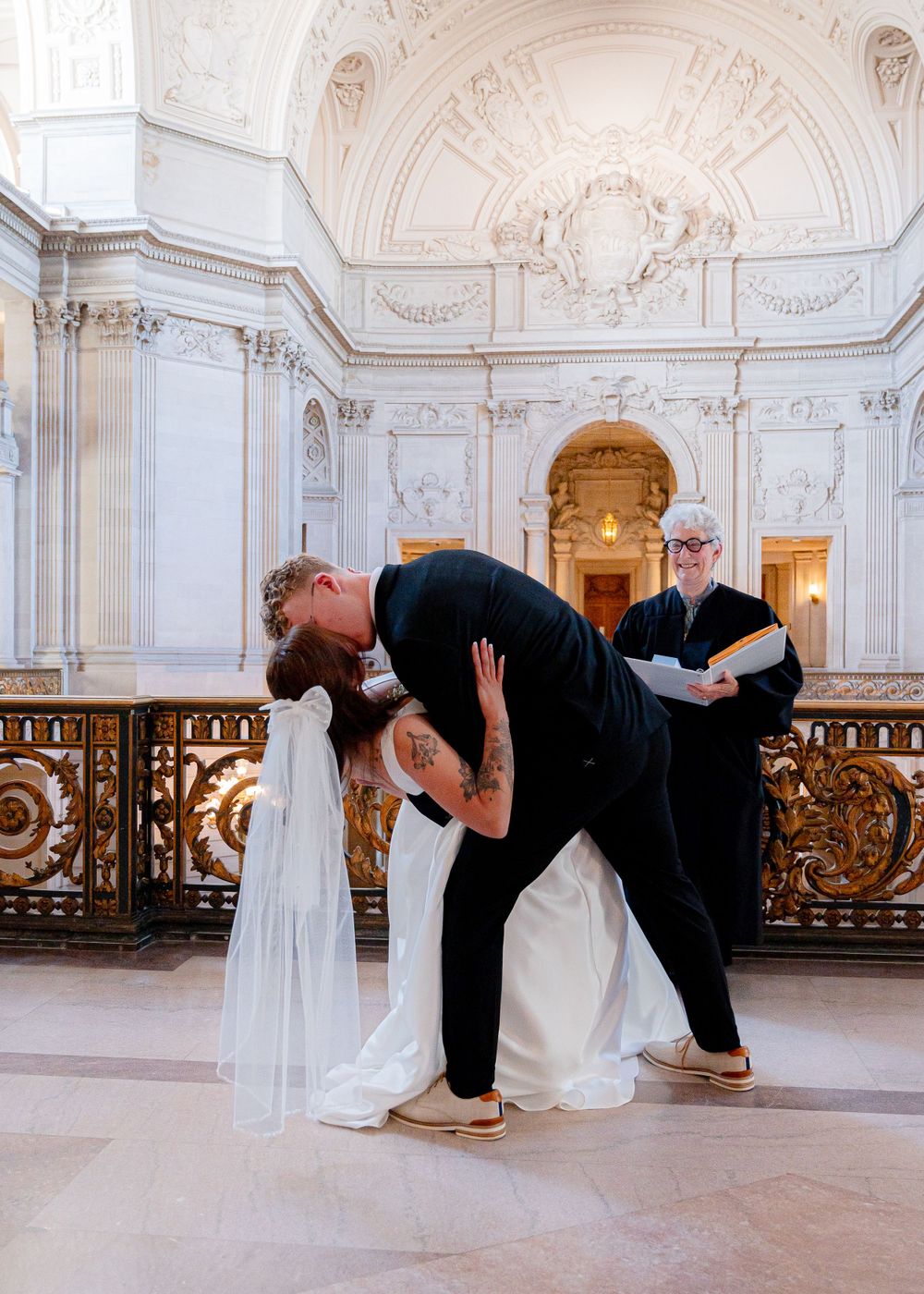 A dramatic wedding photo showing a romantic dip pose in an ornate marble hall.