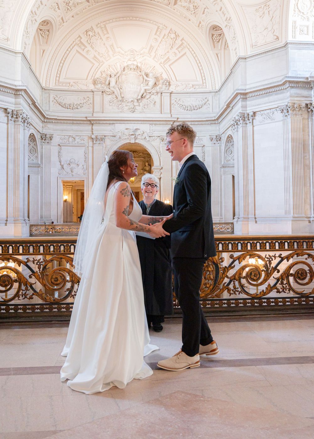 A wedding ceremony taking place in an ornate white marble hall with classical architecture.