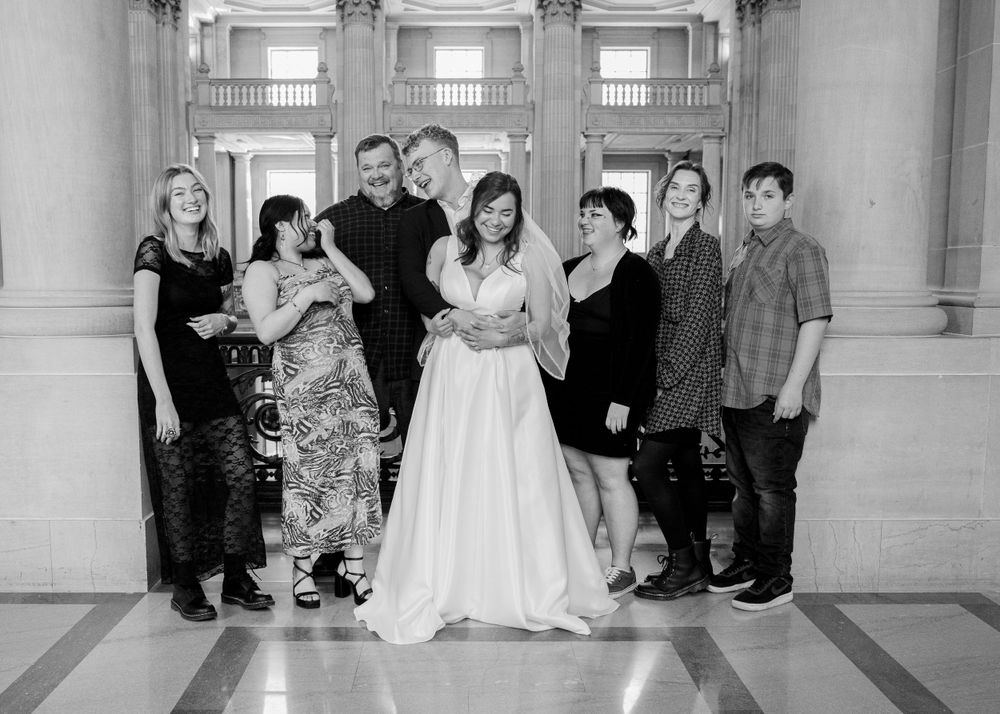 A black and white group portrait of wedding guests and couple in a grand hallway.
