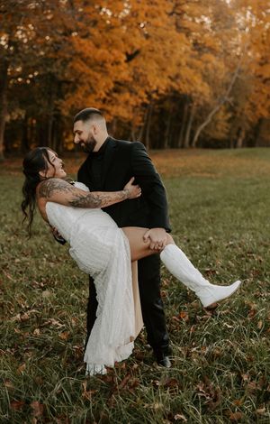 Romantic dance dip pose in a field with autumn trees glowing orange in the background.