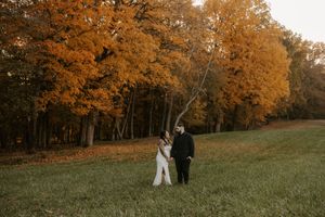 Couple walks together on a path with fall foliage creating a warm autumn backdrop.