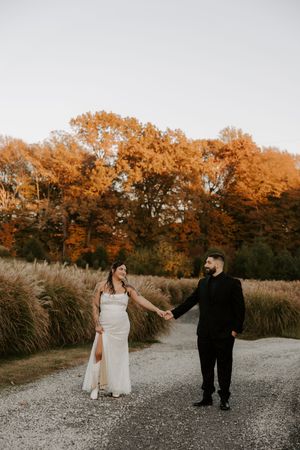 Newlyweds share a moment on a gravel path surrounded by autumn foliage and ornamental grasses.