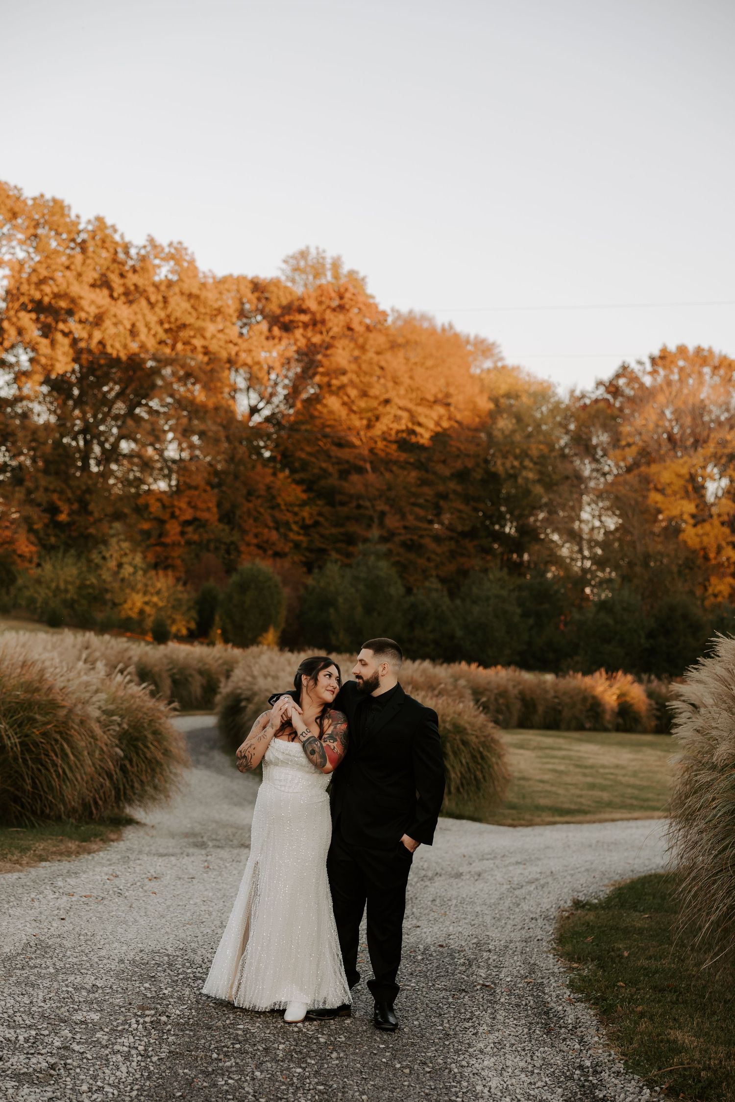 A couple strolls down a winding path with beautiful fall colors in the background.