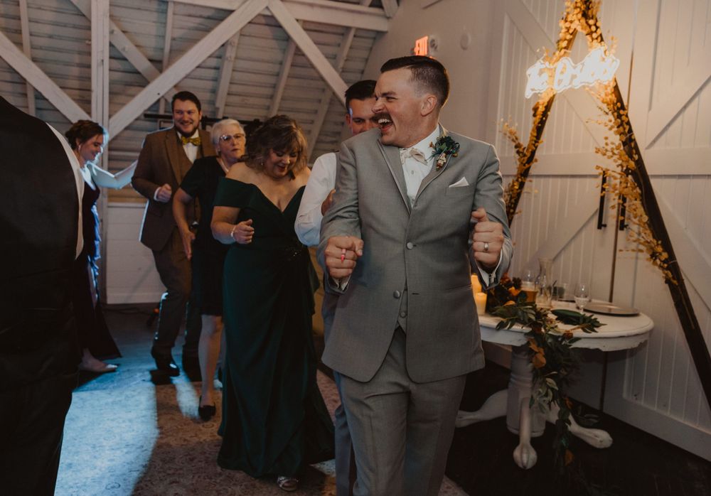 Wedding reception guests dancing and socializing in a rustic barn setting with ambient lighting.