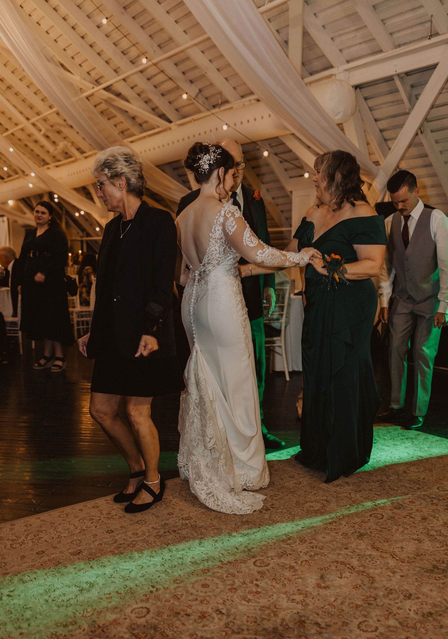 Wedding reception dance floor with green uplighting in a rustic barn venue.