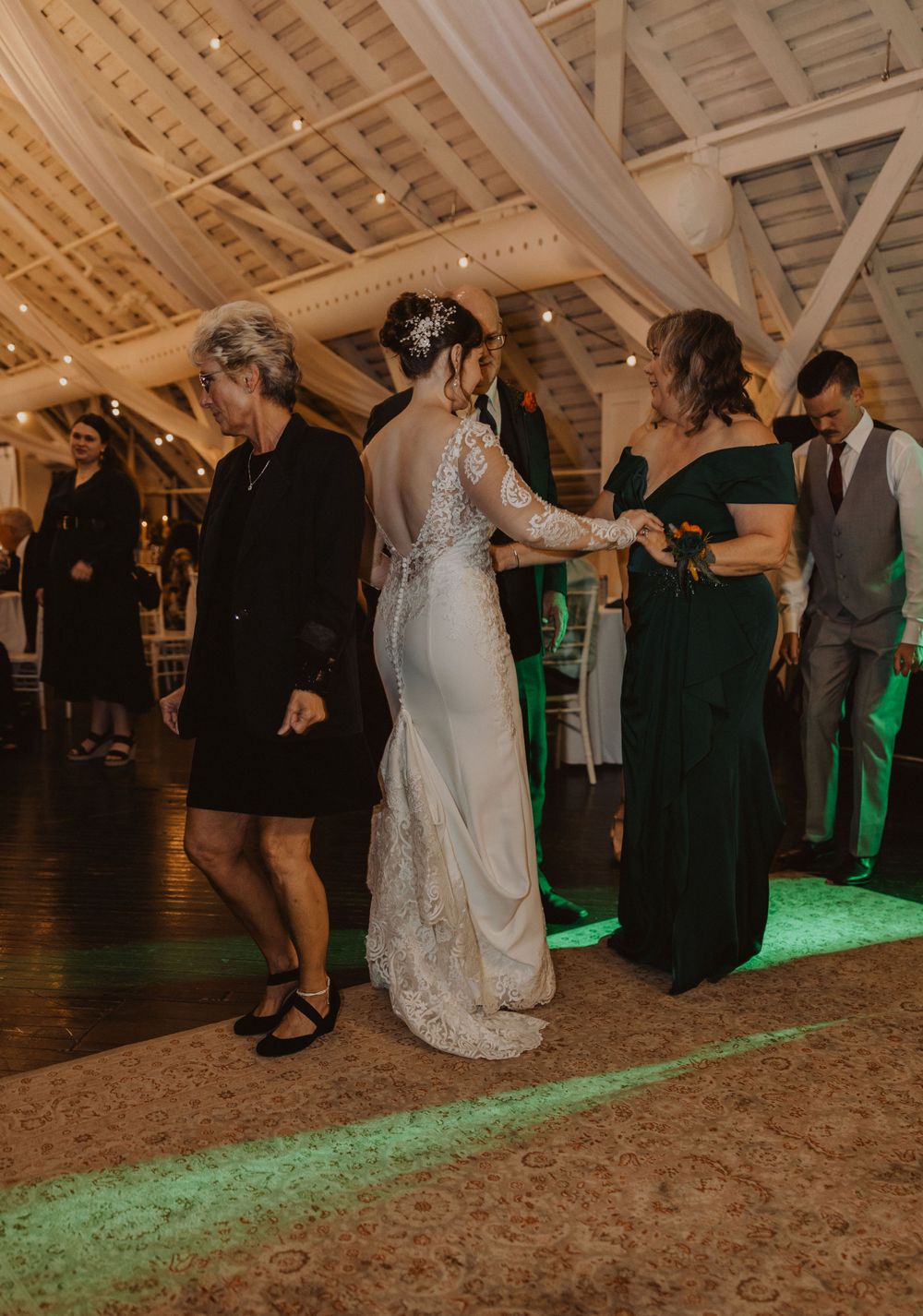 Wedding reception dance floor with green uplighting in a rustic barn venue.