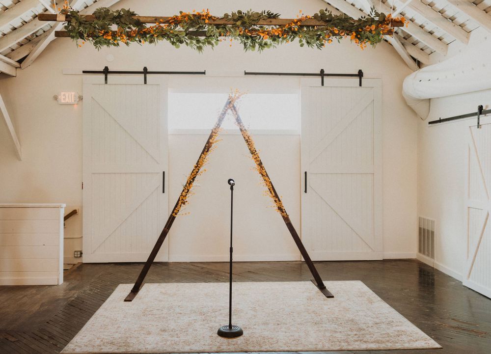 Minimalist wedding ceremony backdrop with crossed wooden beams and floral garland.