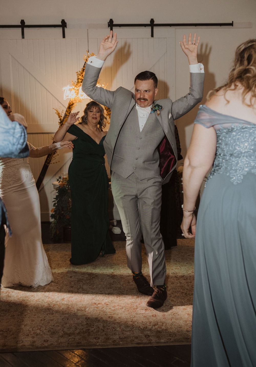 Wedding guests dancing and celebrating in a rustic barn venue with modern lighting.