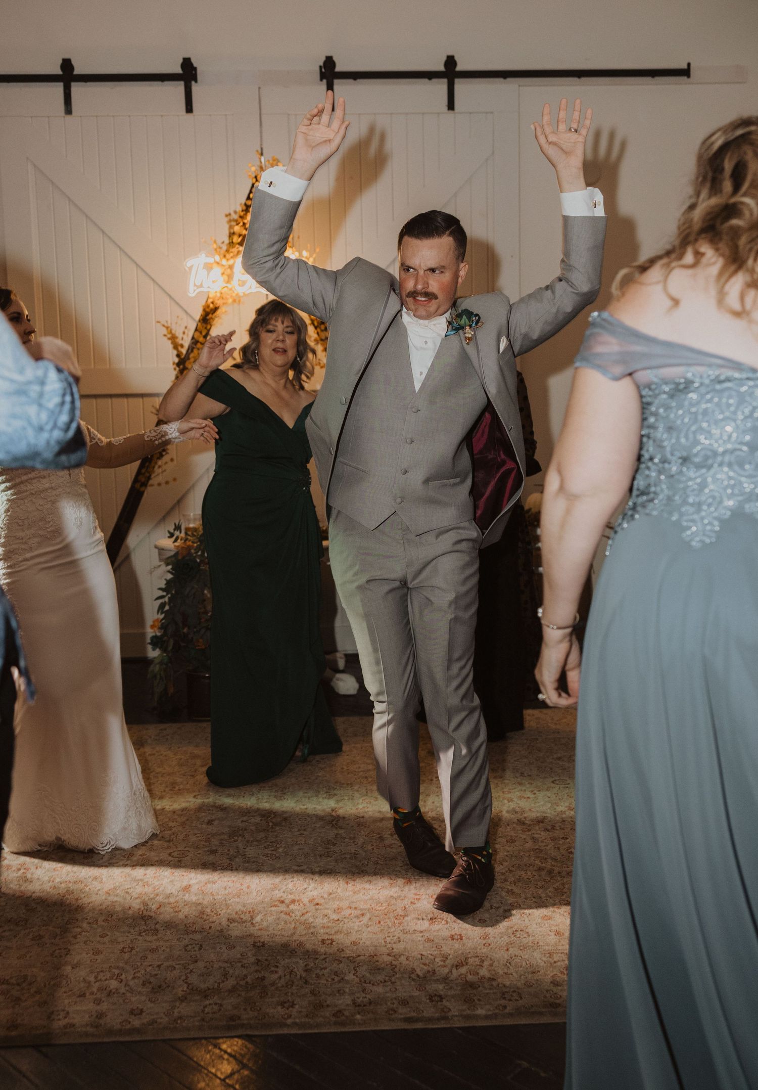 Wedding guests dancing and celebrating in a rustic barn venue with modern lighting.
