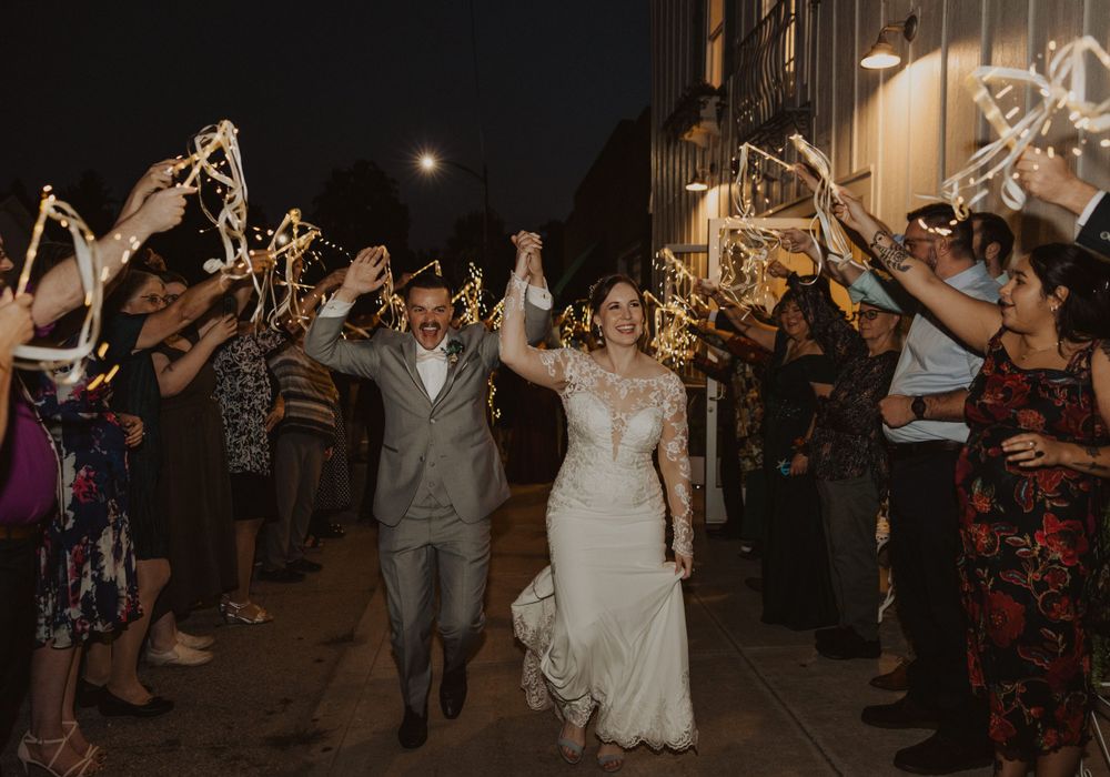 Couple walks through a sparkler tunnel during their wedding exit as guests cheer.