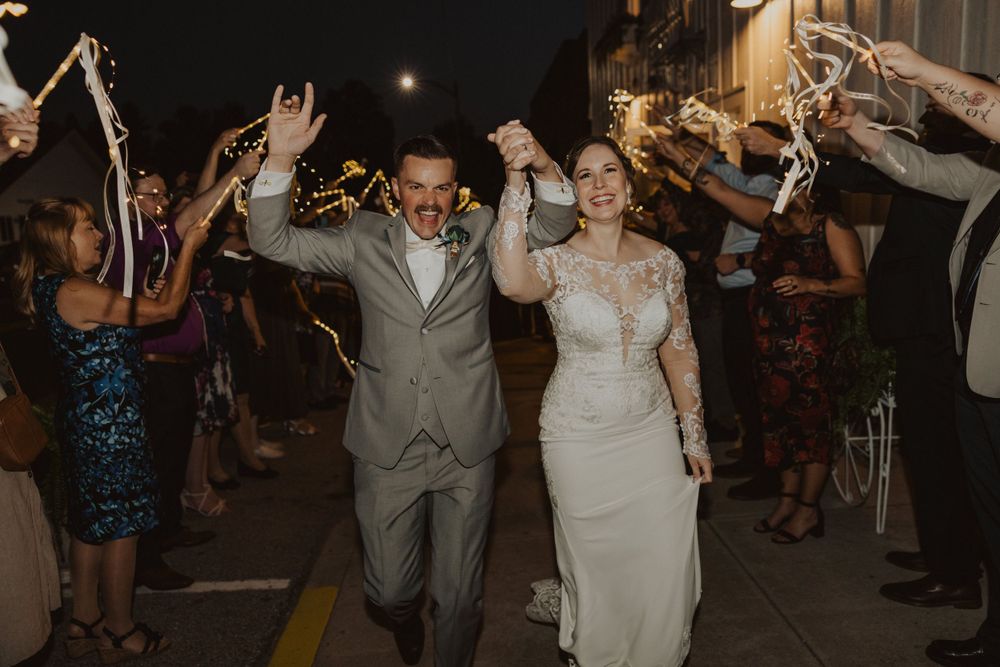 Couple joyfully walks through sparkler tunnel during nighttime wedding celebration.