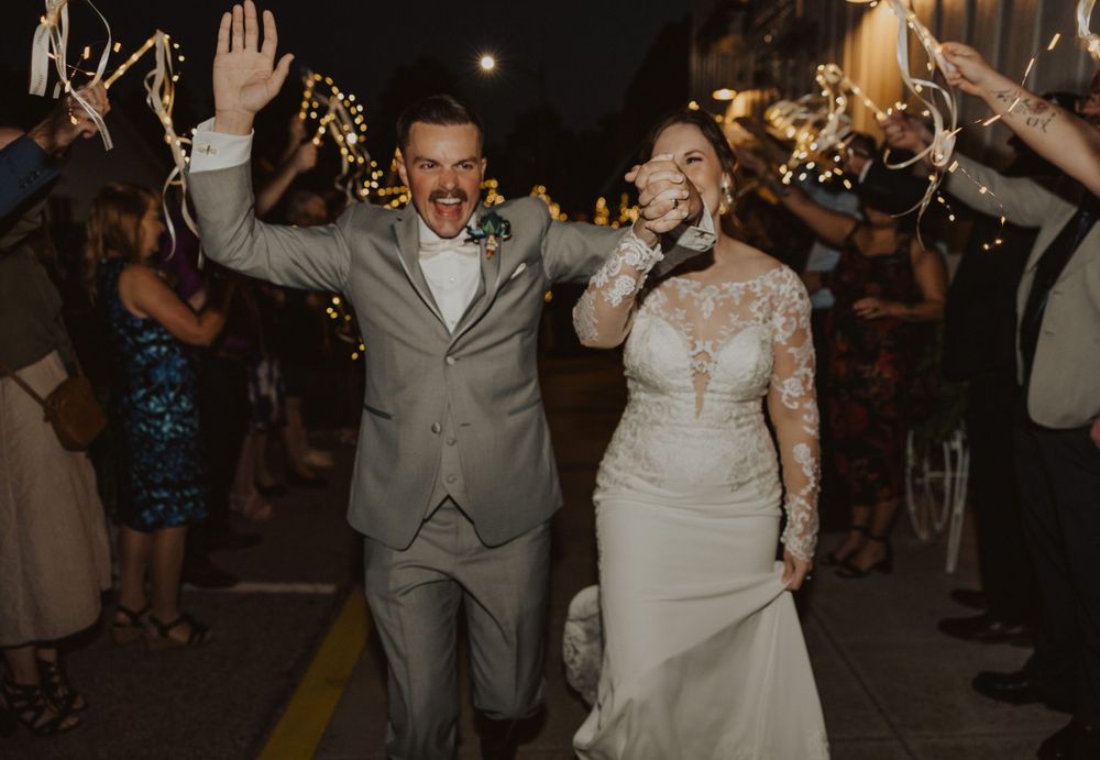 Wedding couple celebrates while walking through sparkler-lined exit path.