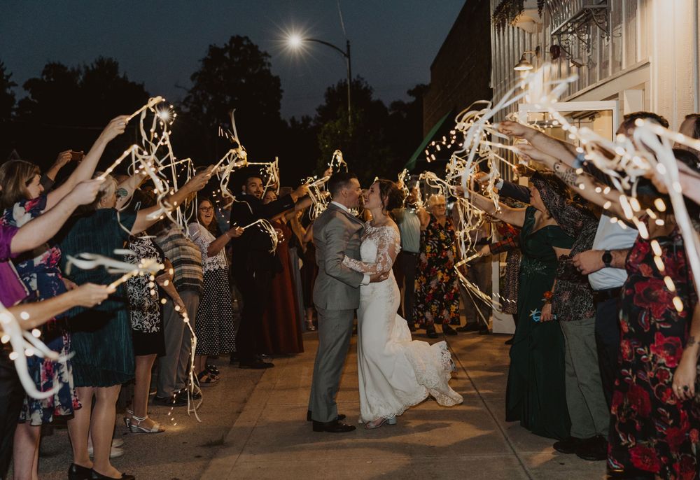 Wedding party creates magical sparkler exit arch for couple during nighttime celebration.
