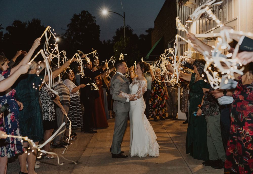 Guests line pathway with glowing sparklers as couple celebrates during evening wedding exit.