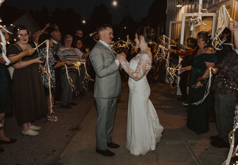 Couple stands together while guests create sparkler tunnel during evening reception exit.