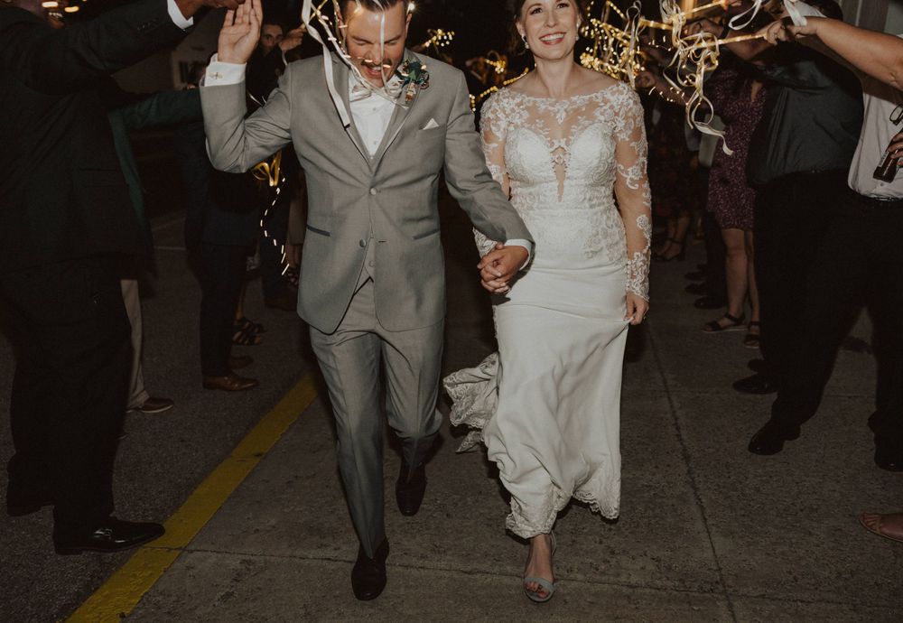 Newlyweds walk hand in hand through a sparkler exit tunnel in elegant wedding attire.