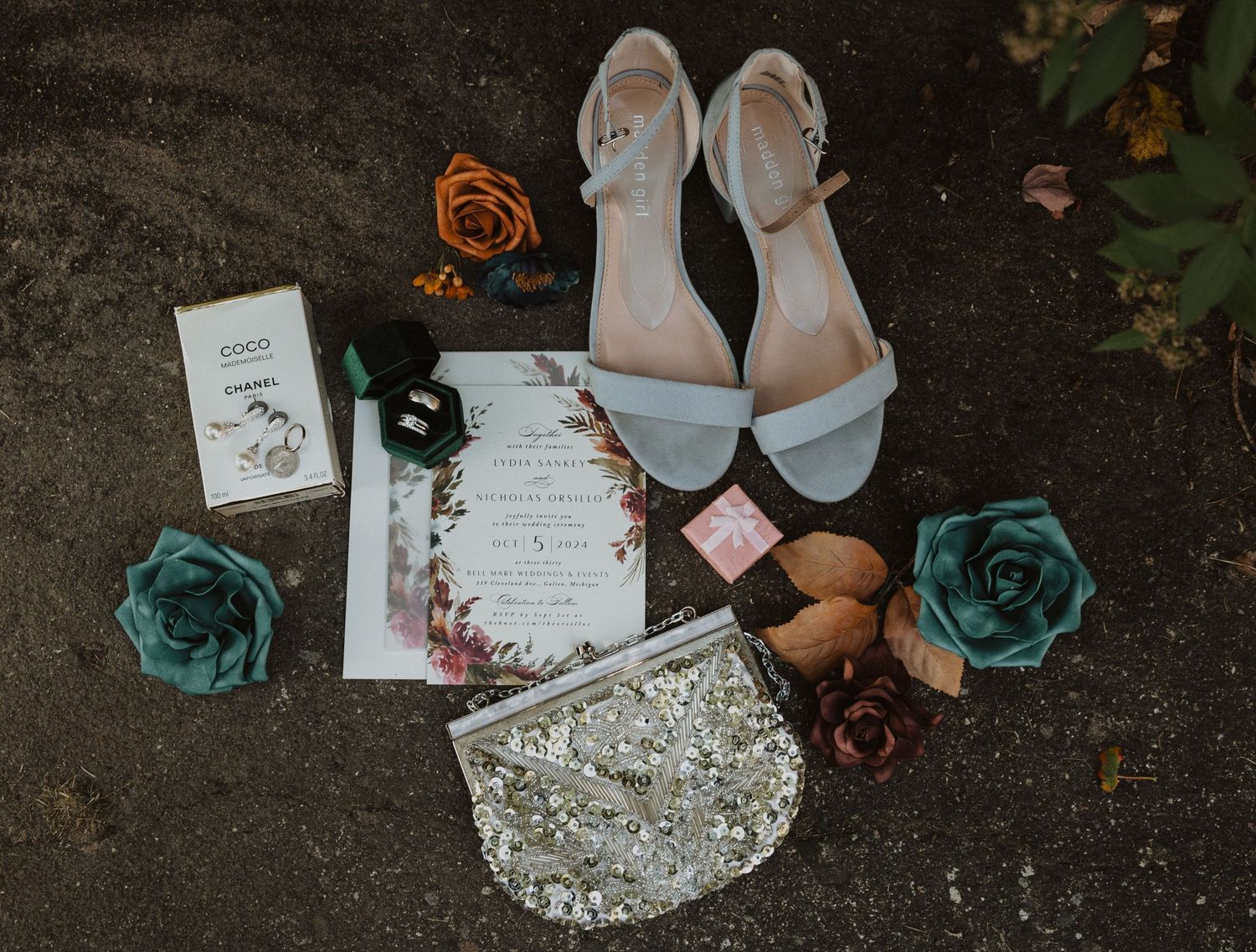 Wedding details including invitations, jewelry and decor arranged on dark surface.