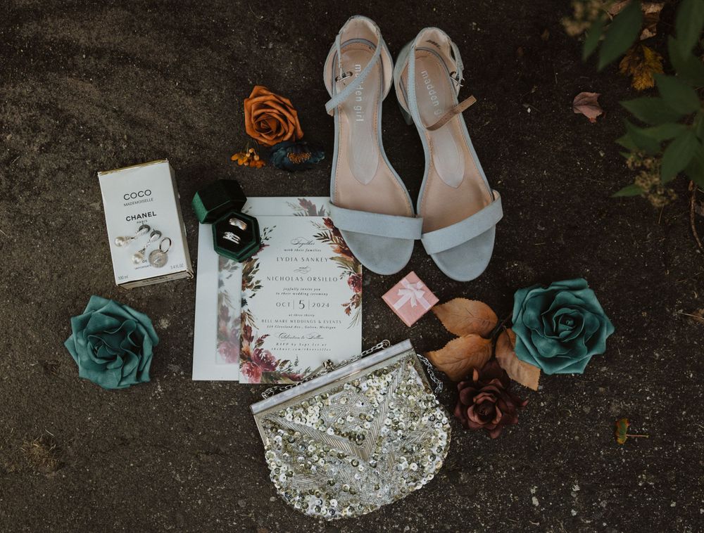 Wedding details including invitations, jewelry and decor arranged on dark surface.