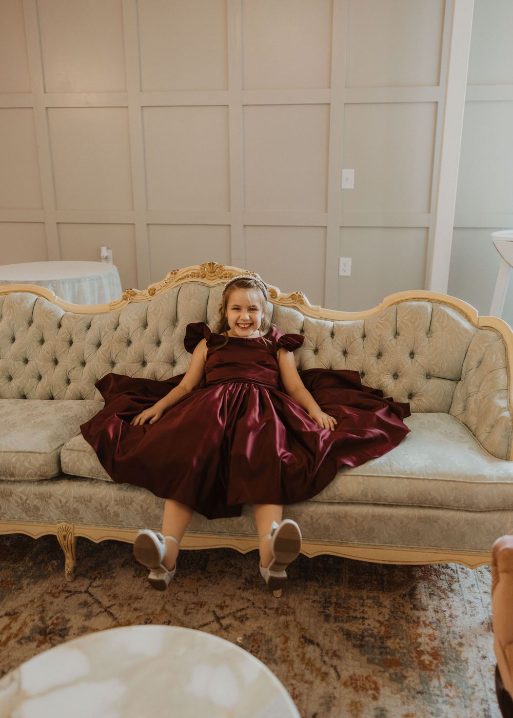 Young attendant in burgundy dress sitting on vintage tufted sofa.