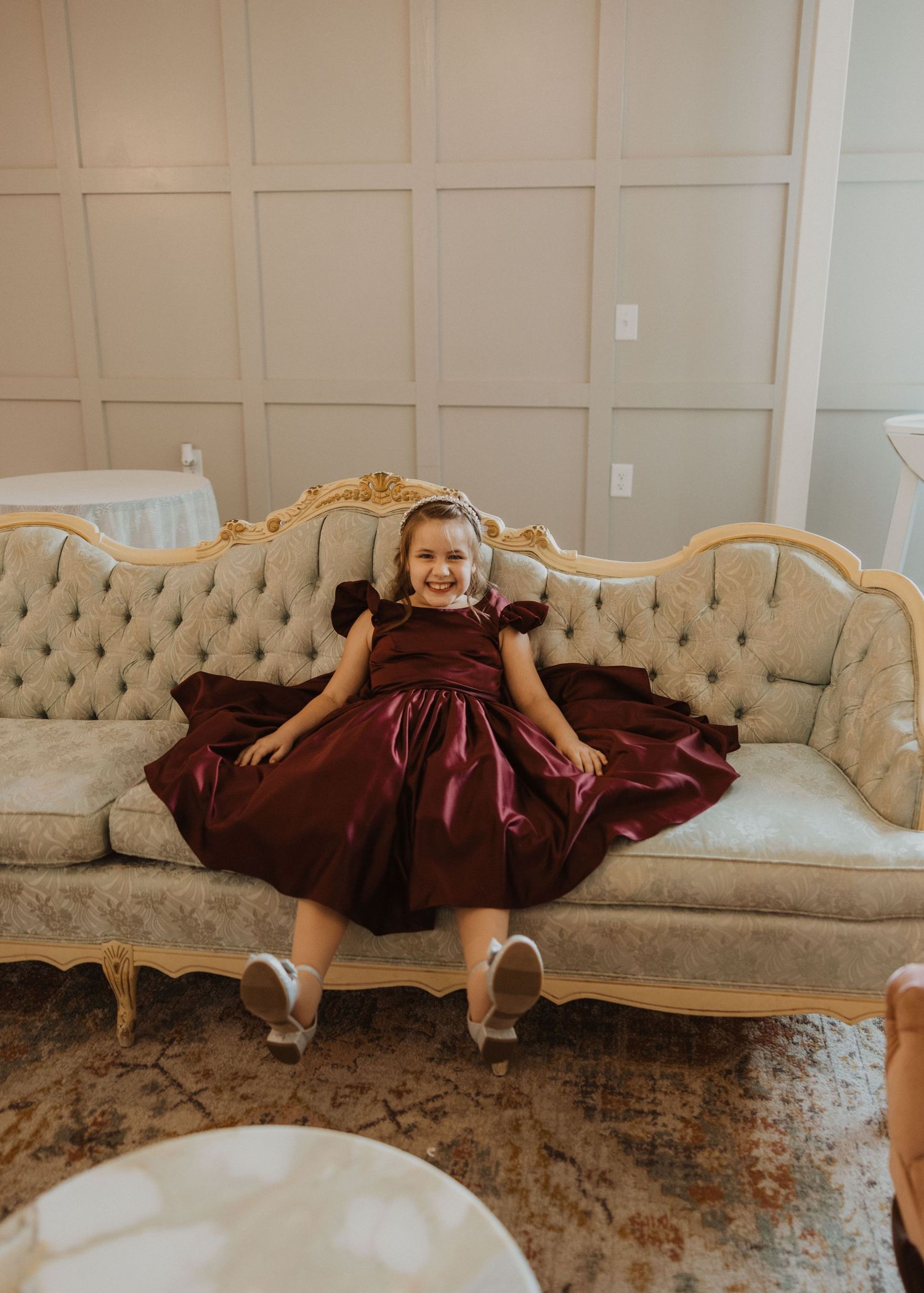 Young attendant in burgundy dress sitting on vintage tufted sofa.