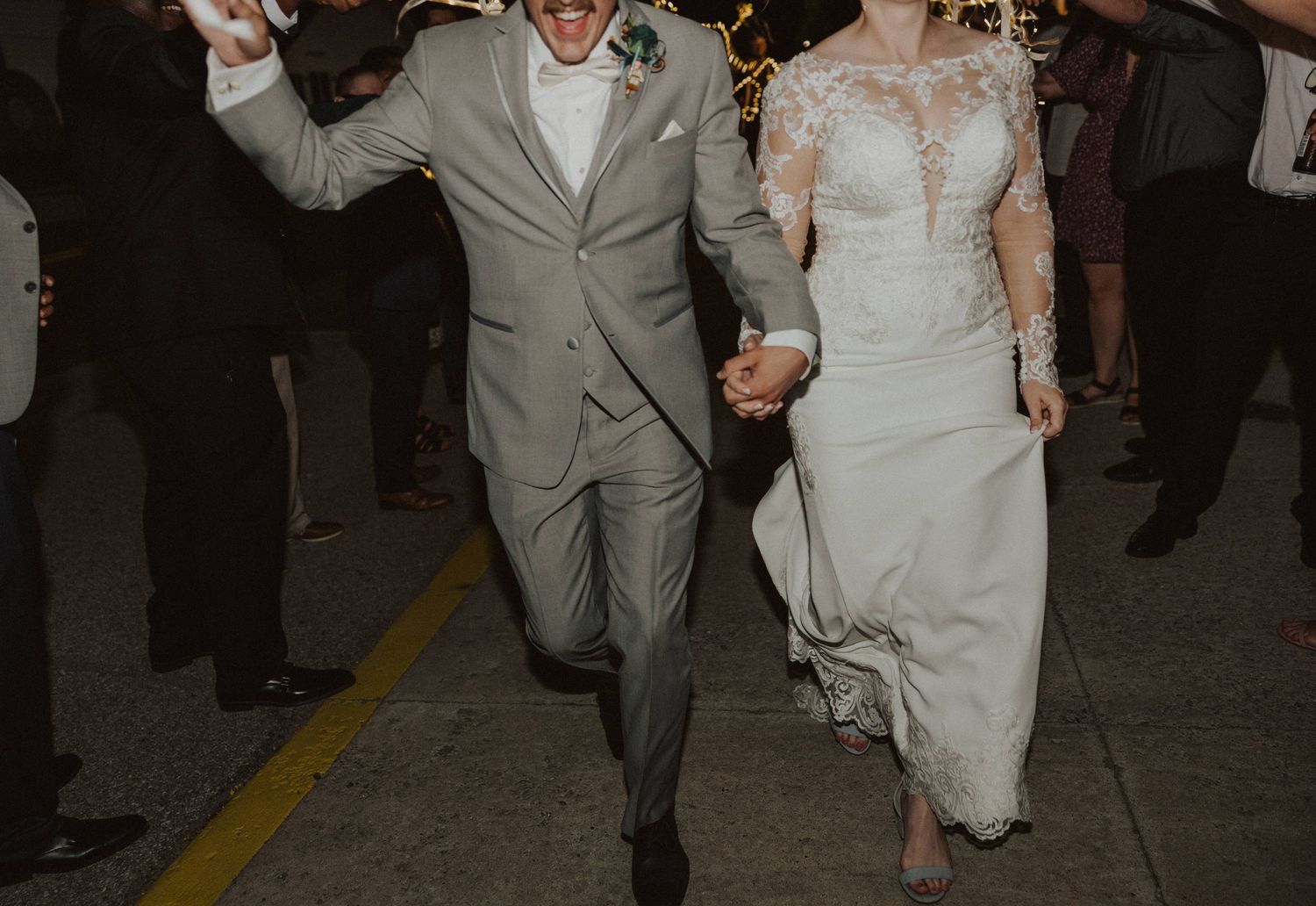 A joyful couple makes their grand exit through sparklers held by wedding guests at night.