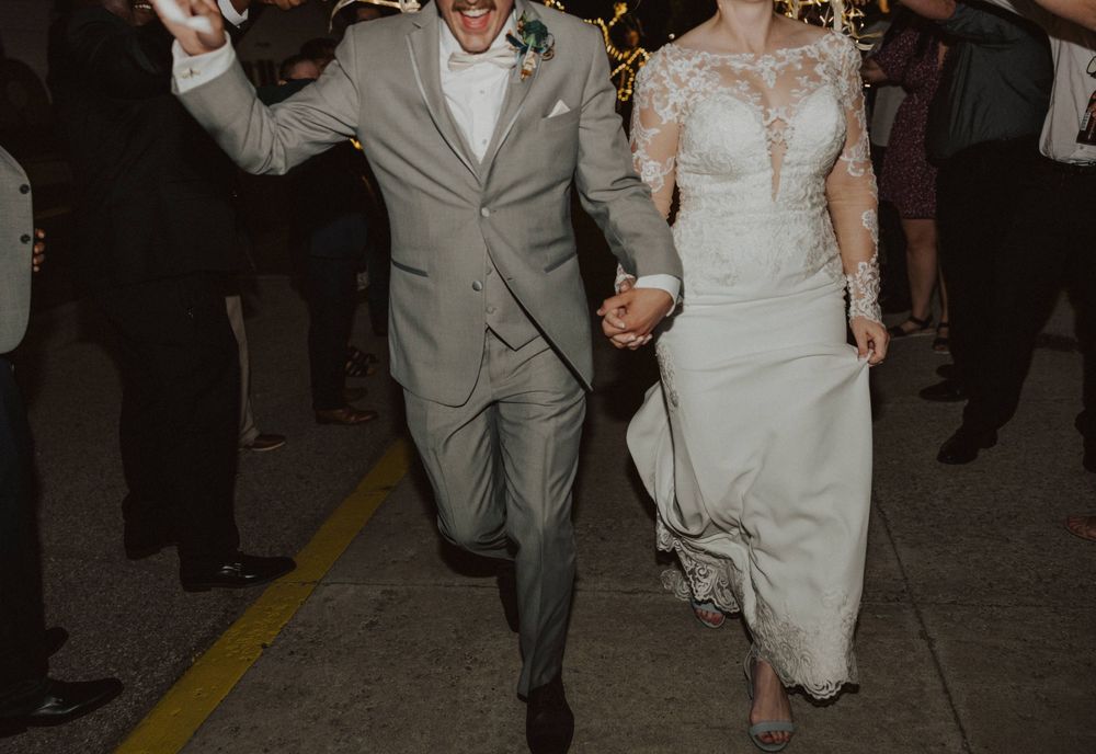 A joyful couple makes their grand exit through sparklers held by wedding guests at night.