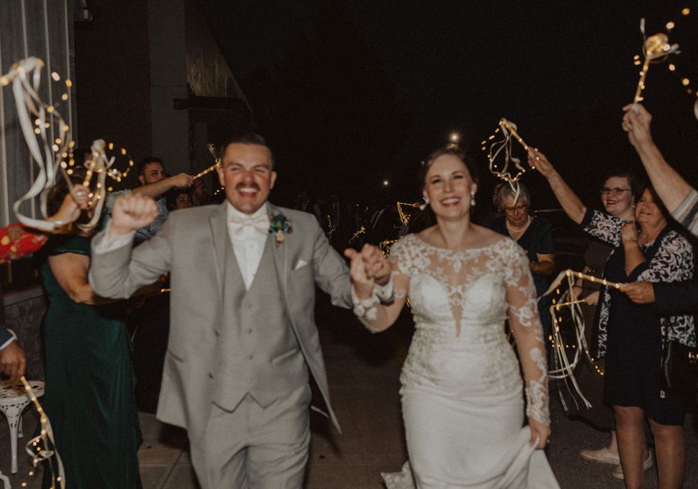 A couple celebrates with raised arms while walking through their wedding sparkler exit.
