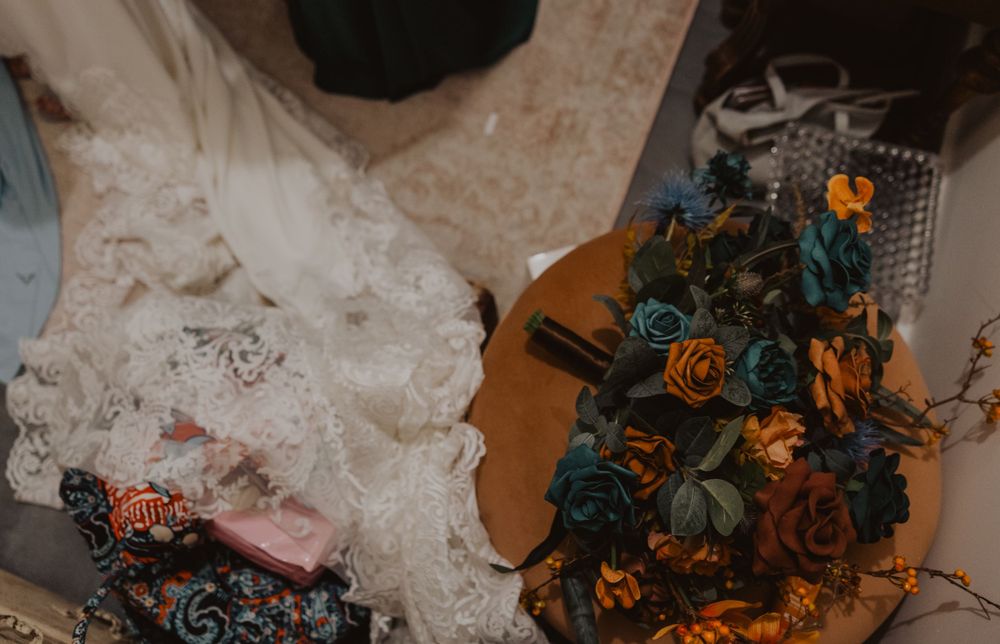 Colorful autumn wedding bouquet with orange and teal flowers arranged on white lace.