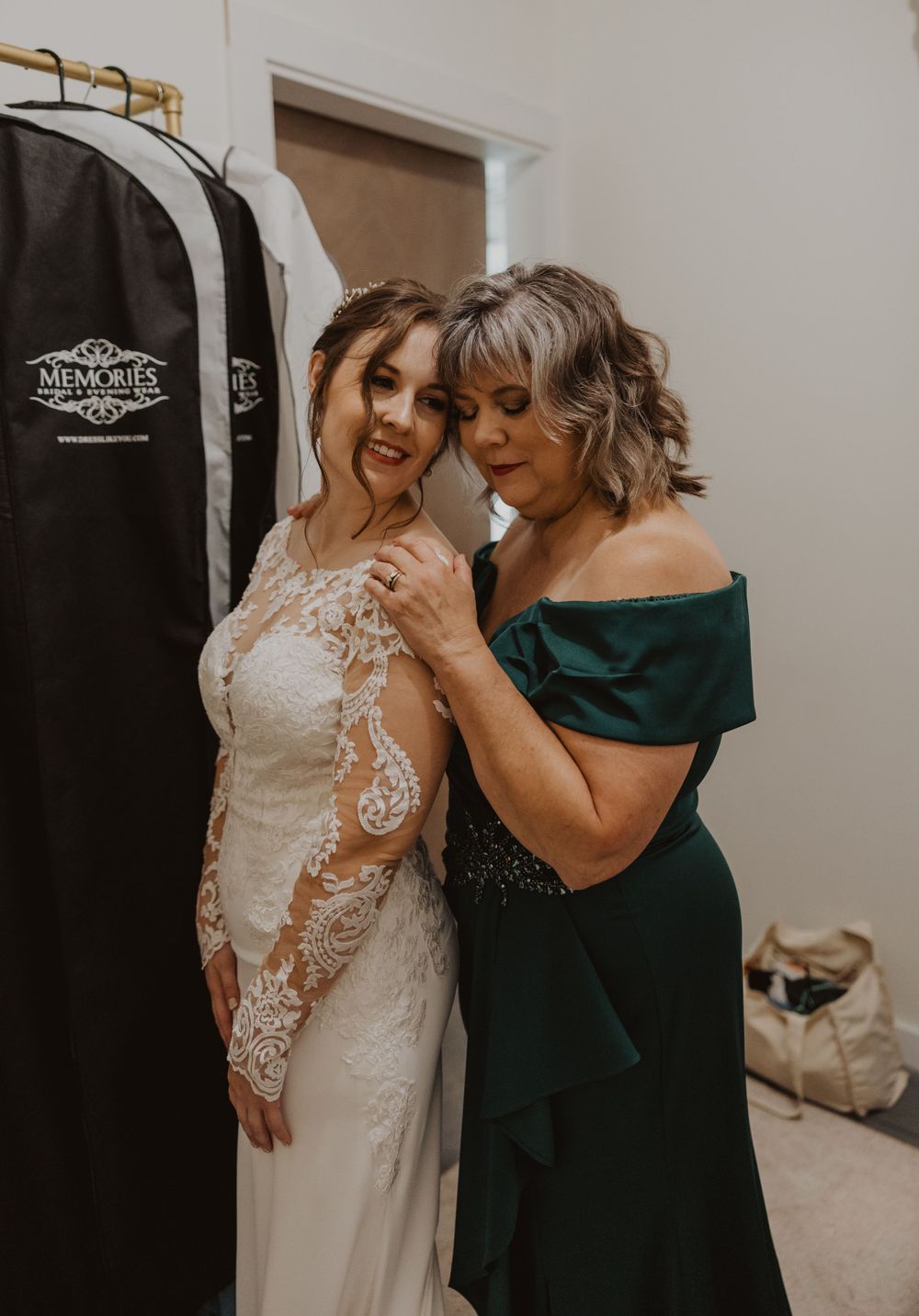 Intimate wedding dress fitting moment with emerald green bridesmaid dress visible.