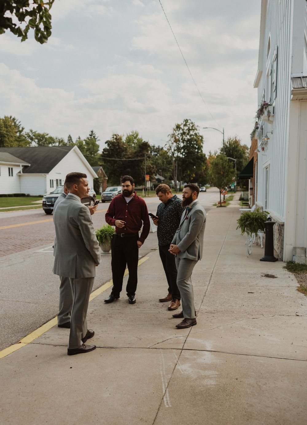 Wedding party in gray suits gathering outside white church building.