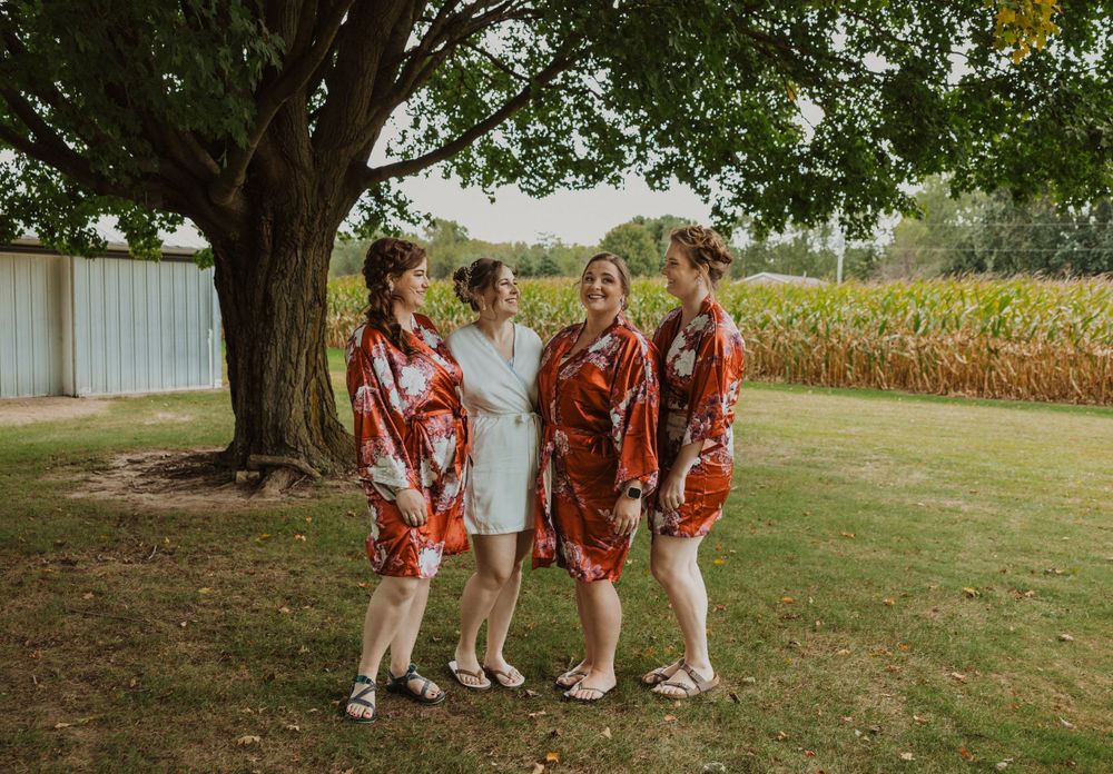 Wedding party gathered under large tree in countryside setting.