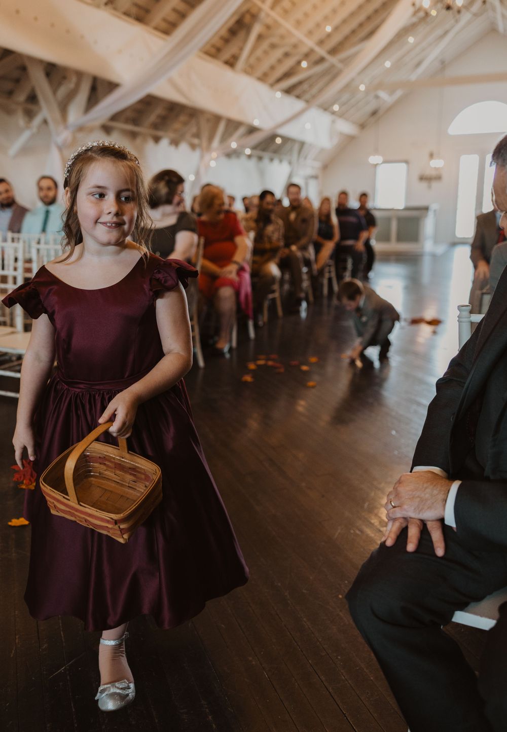 Young flower girls in burgundy dresses carry baskets down the aisle during a wedding ceremony.