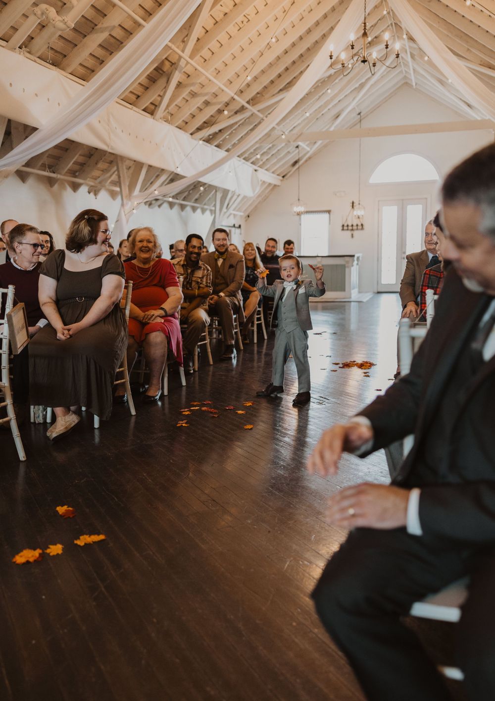 Wedding guests line the sides of a spacious venue with vaulted ceilings and hardwood floors.