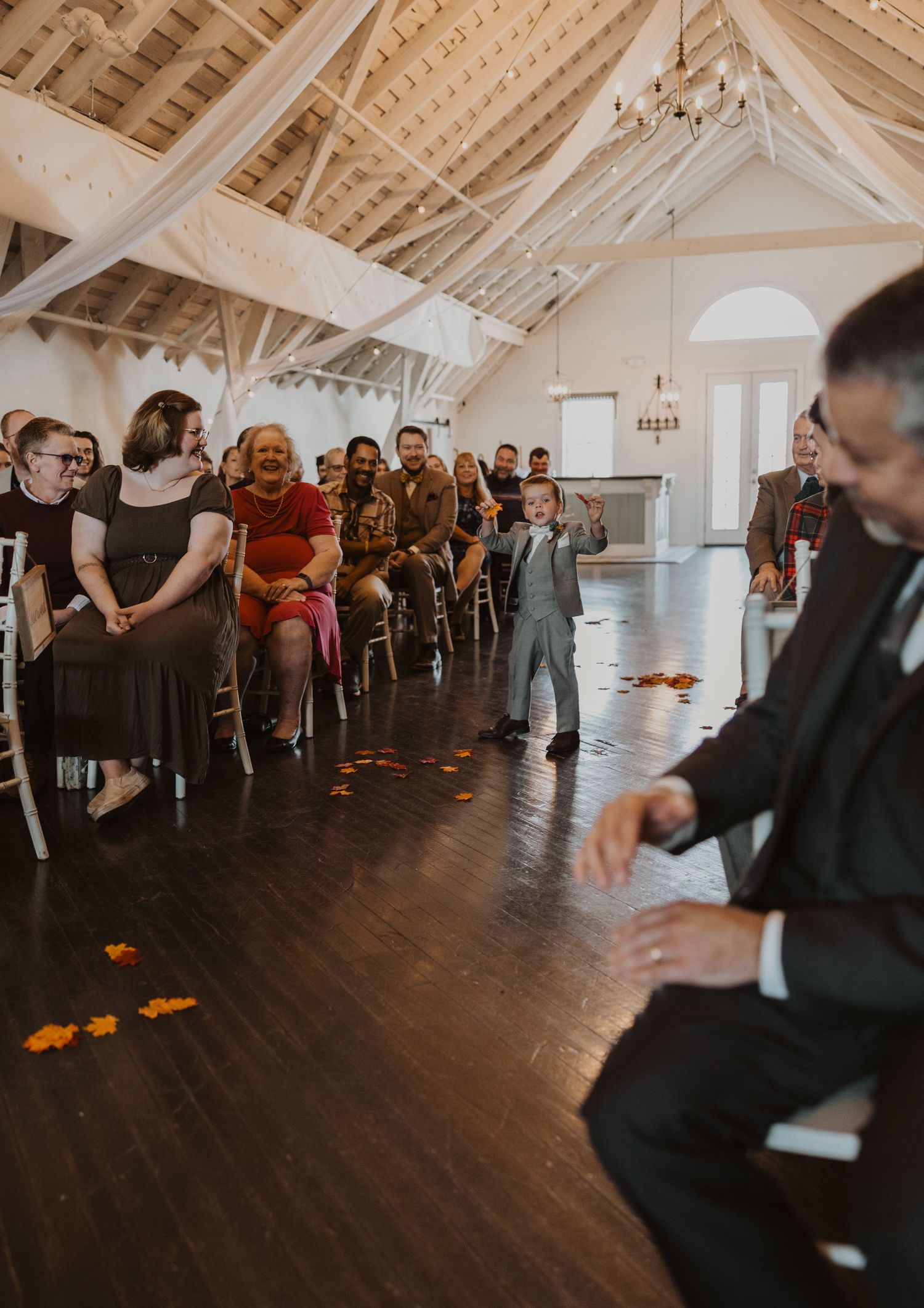 Wedding guests line the sides of a spacious venue with vaulted ceilings and hardwood floors.