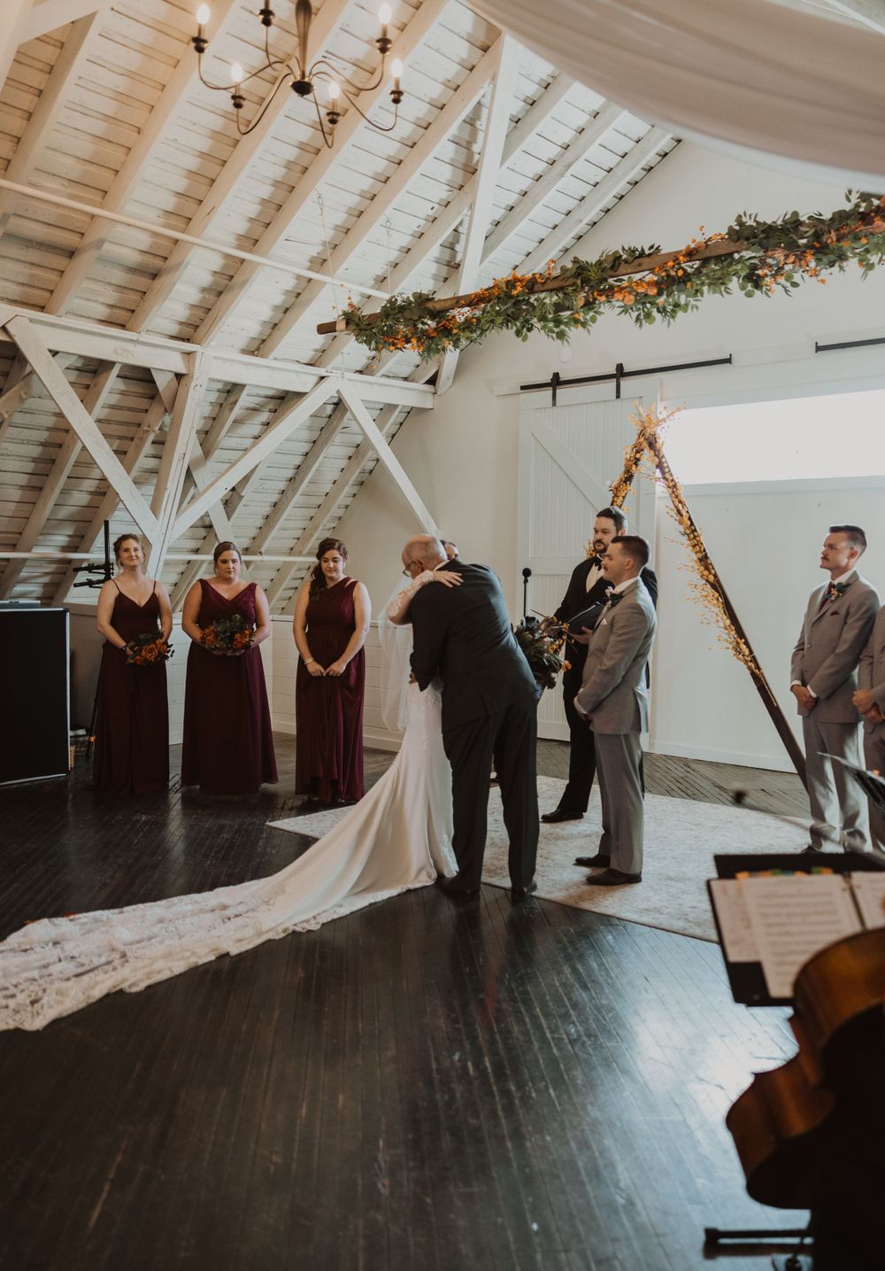 Wedding ceremony setup in a rustic white venue with floral garlands and dark wood floors.