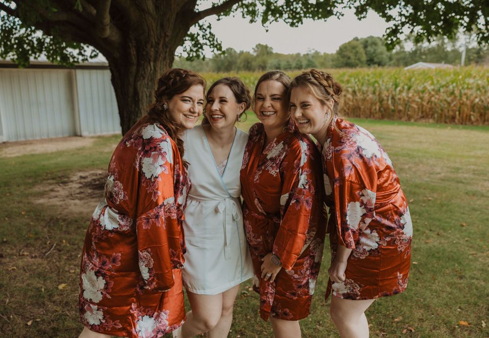 Wedding party in red floral dresses poses together outdoors.