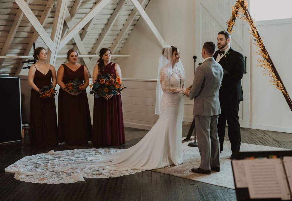 Wedding ceremony in a bright white barn venue with greenery garland decorations and dark wood floors.