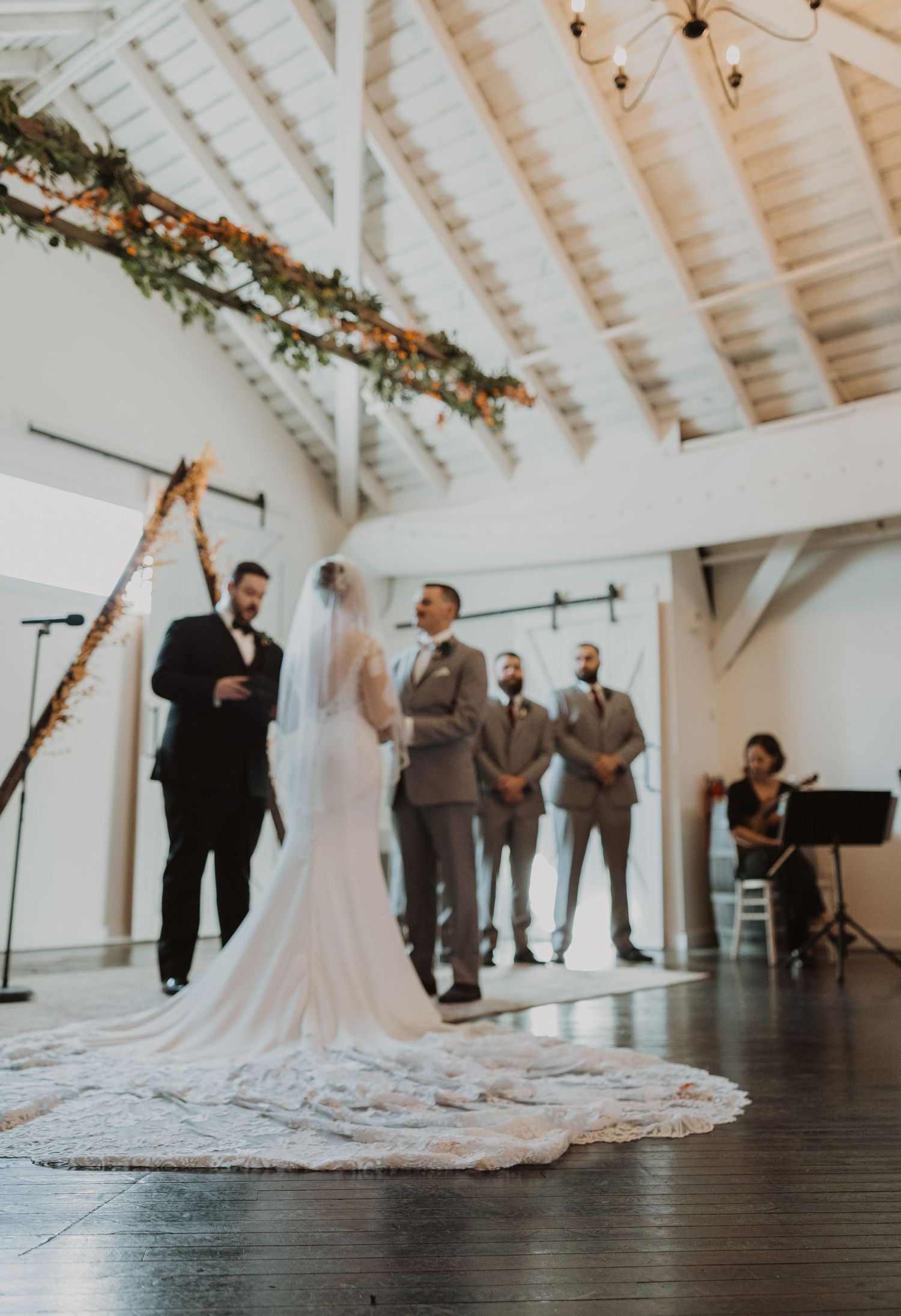 Wedding ceremony setup in modern white barn venue with dramatic lighting and wooden floors.