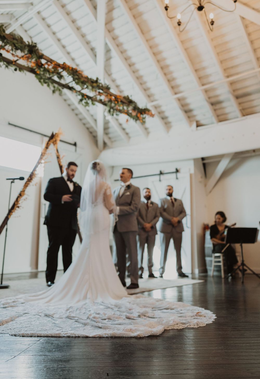 Wedding ceremony setup in modern white barn venue with dramatic lighting and wooden floors.