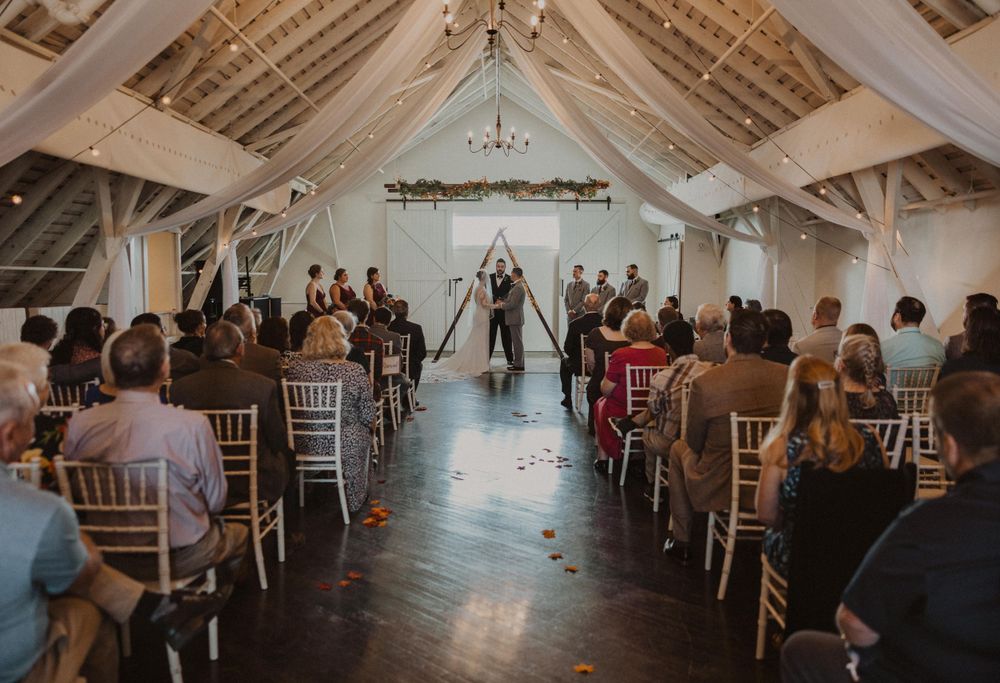 Wedding guests seated in rustic barn venue with vaulted ceilings and chandelier lighting.