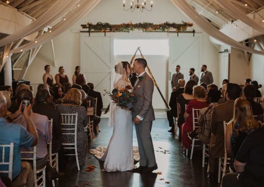Wedding celebration in rustic white barn venue with chandelier and floral ceiling decor.